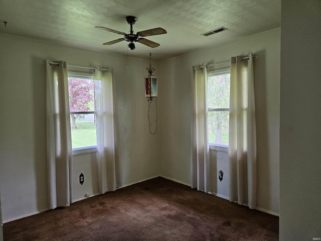 unfurnished room featuring visible vents, a ceiling fan, plenty of natural light, and dark carpet