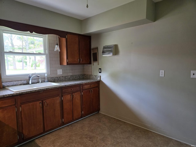 kitchen with baseboards, brown cabinetry, a sink, decorative backsplash, and dark floors