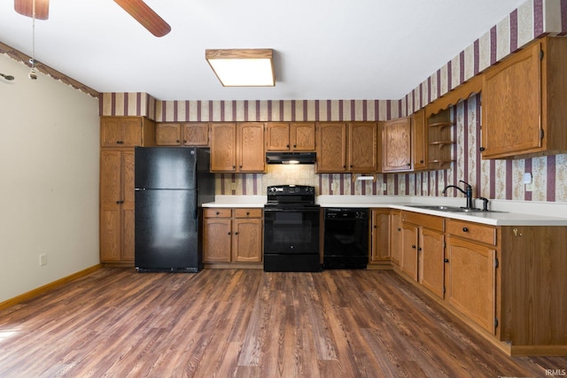 kitchen featuring under cabinet range hood, brown cabinets, black appliances, and a sink