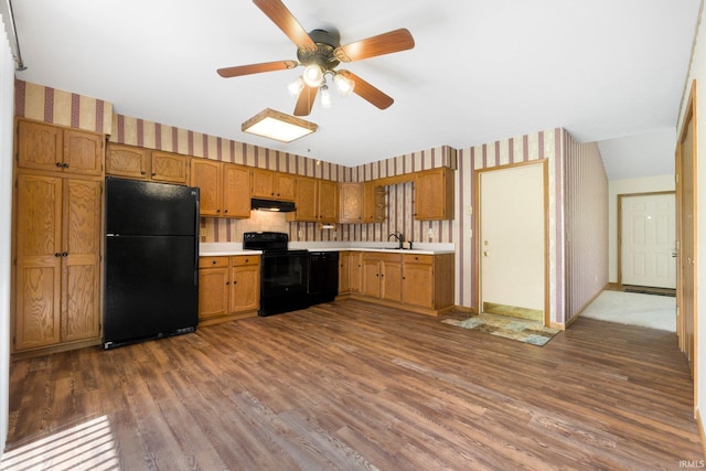 kitchen with a sink, wallpapered walls, black appliances, under cabinet range hood, and light countertops