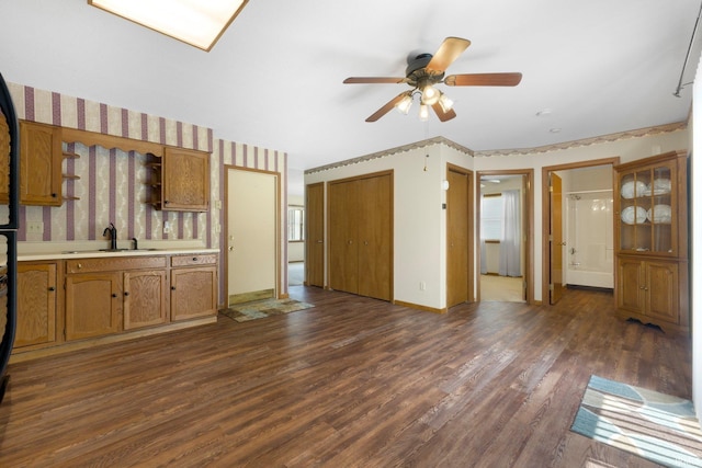 unfurnished living room with baseboards, a sink, ceiling fan, and dark wood-style floors