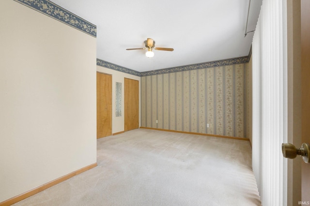 carpeted empty room featuring wallpapered walls, baseboards, and a ceiling fan