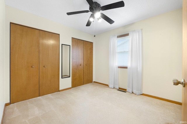 unfurnished bedroom with light colored carpet, multiple closets, visible vents, a ceiling fan, and baseboards