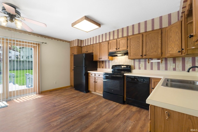 kitchen with a sink, dark wood finished floors, black appliances, under cabinet range hood, and light countertops