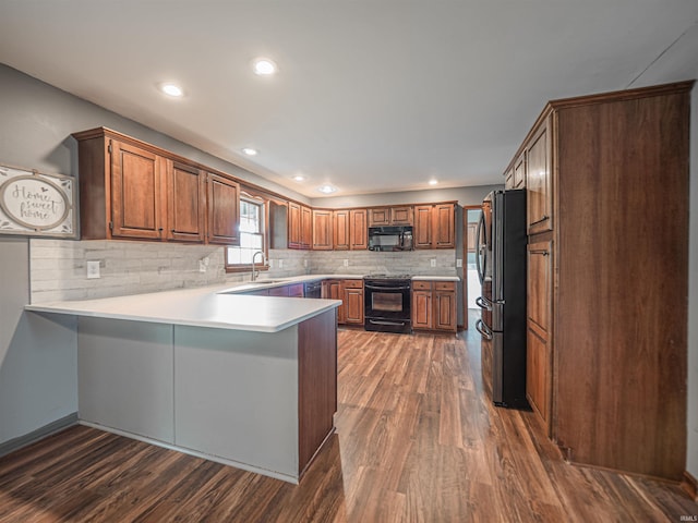 kitchen featuring a peninsula, dark wood finished floors, black appliances, and a sink