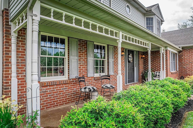 doorway to property with covered porch, roof with shingles, and brick siding