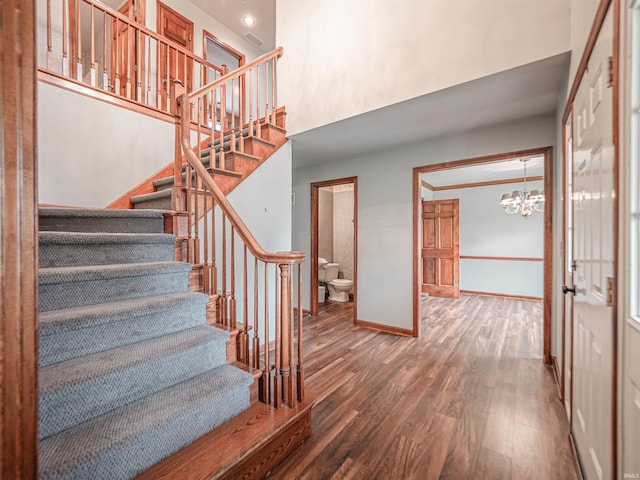 stairs with a towering ceiling, a chandelier, wood finished floors, and baseboards