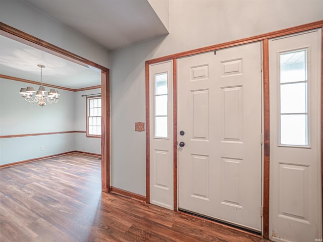 foyer entrance featuring dark wood-style flooring, ornamental molding, baseboards, and a notable chandelier
