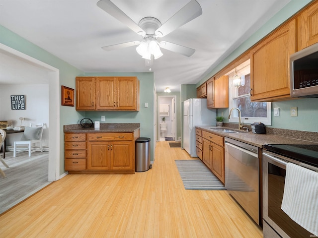 kitchen with light wood finished floors, a ceiling fan, a sink, stainless steel appliances, and brown cabinetry