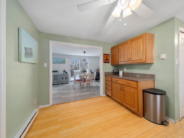 kitchen featuring a baseboard radiator, ceiling fan, baseboards, dark countertops, and light wood-style floors