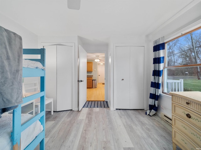 unfurnished bedroom with baseboard heating, multiple closets, and light wood-style flooring