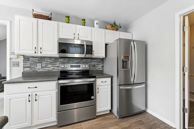 kitchen with dark countertops, stainless steel appliances, dark wood-style flooring, and backsplash