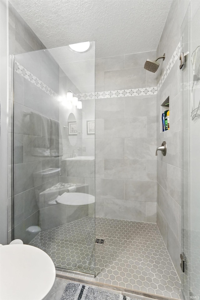 bathroom with a textured ceiling, toilet, and a shower stall