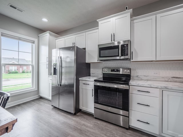 kitchen featuring tasteful backsplash, visible vents, light wood-style floors, stainless steel appliances, and white cabinets