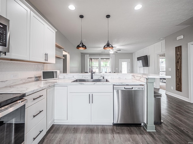 kitchen with a sink, a peninsula, dark wood-type flooring, stainless steel appliances, and white cabinets