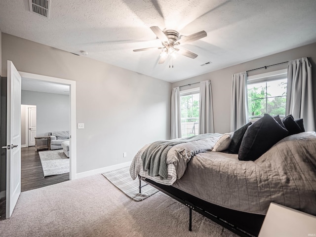 carpeted bedroom with ceiling fan, a textured ceiling, baseboards, and visible vents
