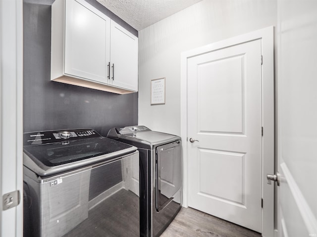 laundry area featuring cabinet space, washing machine and clothes dryer, light wood-style floors, and a textured ceiling