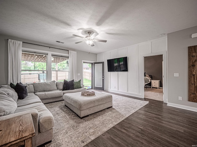 living area with a textured ceiling, dark wood-type flooring, visible vents, a ceiling fan, and baseboards
