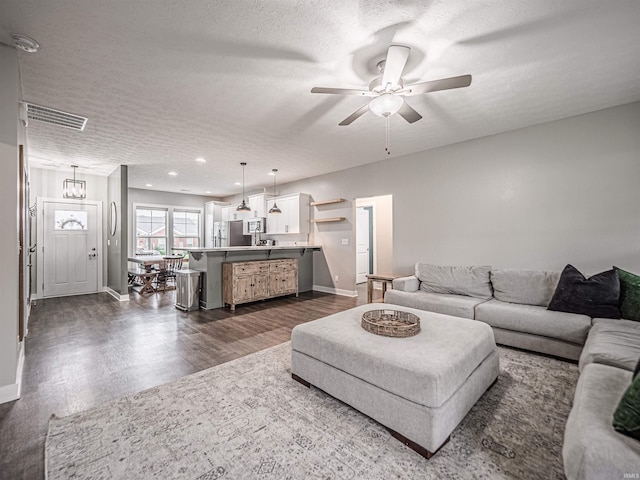 living room with dark wood finished floors, visible vents, baseboards, a textured ceiling, and ceiling fan