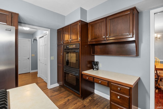 5259 E Willow Ct, Monticello, IN 47960 - kitchen featuring freestanding refrigerator, dark wood-style flooring, built in study area, dobule oven black, and light countertops