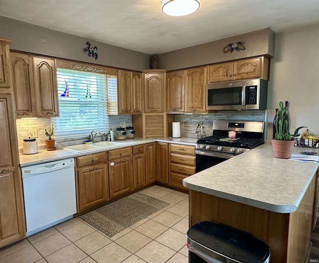kitchen featuring a sink, a peninsula, stainless steel appliances, decorative backsplash, and light countertops