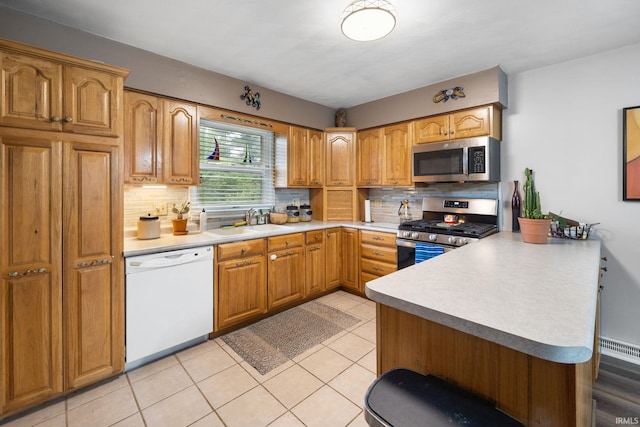 kitchen featuring a peninsula, decorative backsplash, stainless steel appliances, and a sink