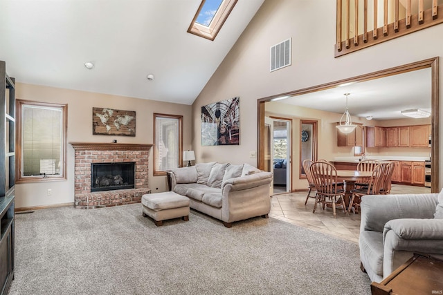living area featuring visible vents, a brick fireplace, high vaulted ceiling, a skylight, and light colored carpet