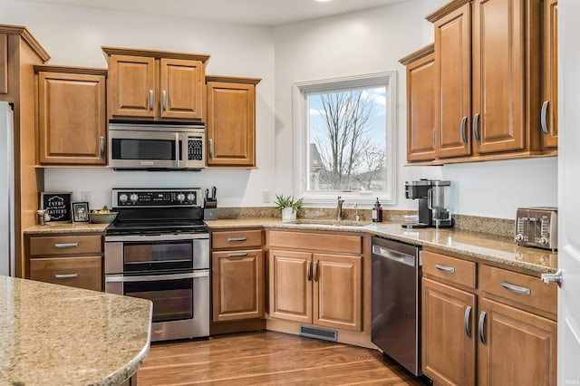 kitchen featuring brown cabinets, a sink, visible vents, light stone countertops, and appliances with stainless steel finishes