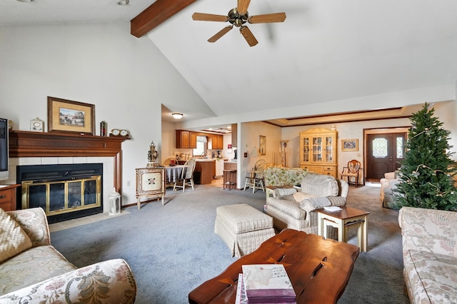 living area featuring a ceiling fan, high vaulted ceiling, a fireplace, beamed ceiling, and light colored carpet
