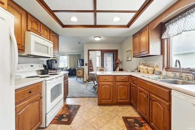 kitchen with a sink, a peninsula, brown cabinetry, white appliances, and light countertops