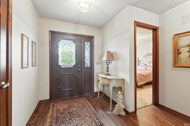 entryway featuring baseboards, visible vents, a textured ceiling, and wood finished floors