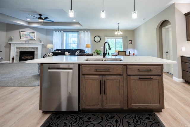 kitchen featuring stainless steel dishwasher, a sink, ceiling fan with notable chandelier, open floor plan, and light wood-type flooring