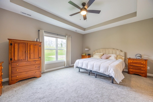 carpeted bedroom with a tray ceiling, visible vents, baseboards, and a ceiling fan