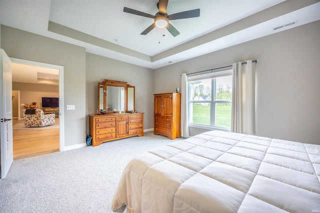 bedroom with a ceiling fan, a tray ceiling, baseboards, visible vents, and light carpet