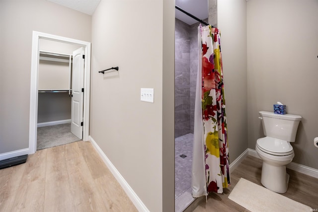 full bathroom featuring toilet, baseboards, wood finished floors, and a tile shower