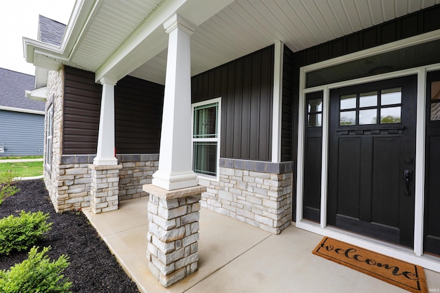 doorway to property with covered porch, stone siding, and board and batten siding