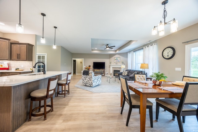 dining area featuring a raised ceiling, light wood finished floors, a fireplace, and ceiling fan