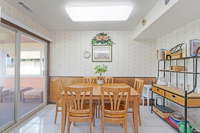 dining room with light tile patterned floors, visible vents, wood walls, and wainscoting