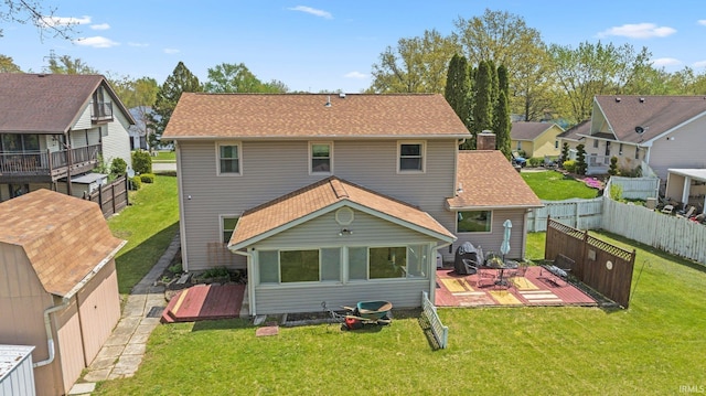 rear view of property with a lawn, a deck, a shingled roof, and fence