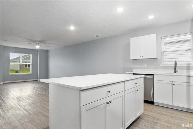 kitchen with a sink, dishwasher, a ceiling fan, a kitchen island, and light wood-style floors