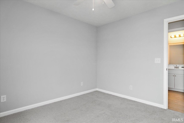 carpeted empty room featuring a ceiling fan, baseboards, and a sink