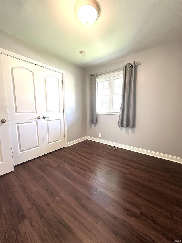 unfurnished bedroom featuring visible vents, baseboards, and dark wood-style floors