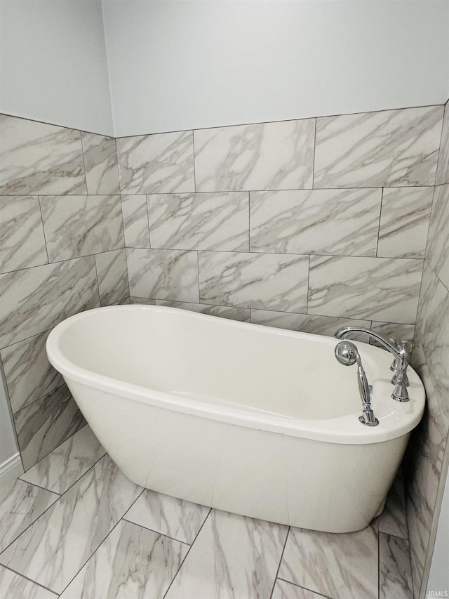 bathroom with marble finish floor and a freestanding tub