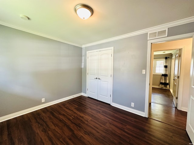 unfurnished bedroom featuring a closet, visible vents, dark wood finished floors, crown molding, and baseboards