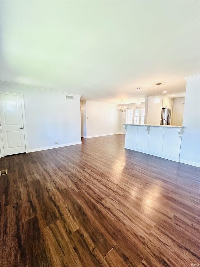 unfurnished living room featuring baseboards, dark wood-style flooring, a notable chandelier, and visible vents