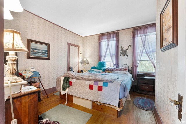 bedroom featuring baseboards, wallpapered walls, and wood finished floors