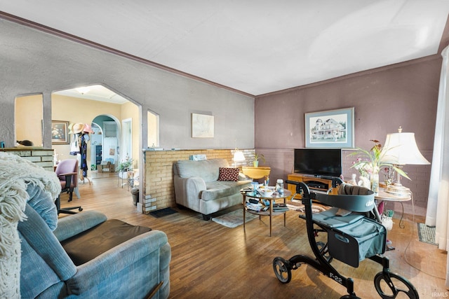living area with arched walkways, crown molding, and wood finished floors