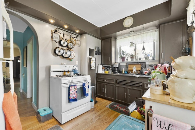 kitchen with dark brown cabinetry, light wood-style flooring, white range with gas cooktop, and arched walkways