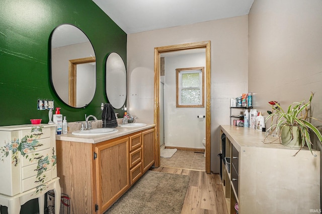 full bath featuring toilet, double vanity, a sink, and wood finished floors