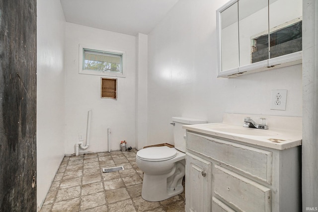 bathroom with vanity, toilet, stone finish floor, and visible vents